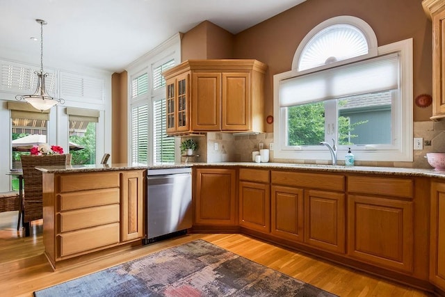 kitchen featuring dishwasher, a sink, light wood finished floors, decorative light fixtures, and backsplash