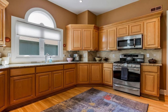 kitchen featuring appliances with stainless steel finishes, light wood-style floors, a sink, and decorative backsplash