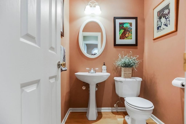 half bathroom with toilet, wood finished floors, and baseboards