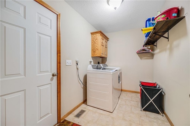 clothes washing area featuring washer and clothes dryer, a textured ceiling, cabinet space, and baseboards