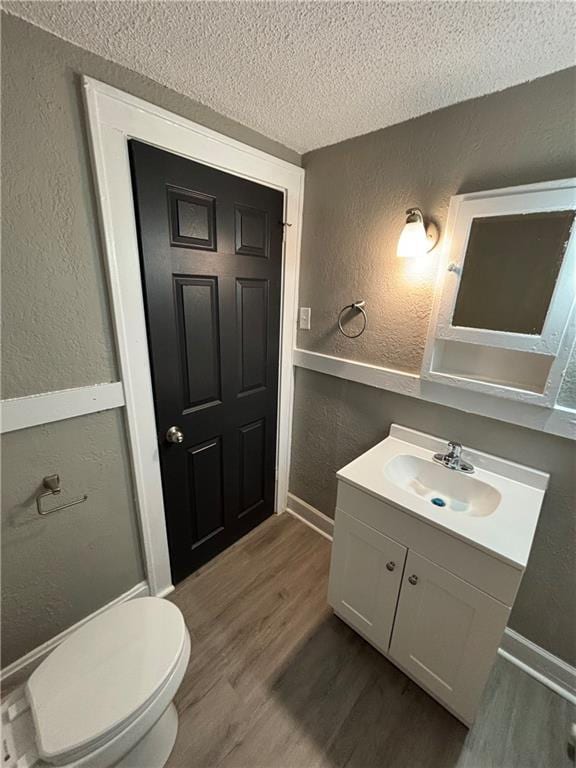 bathroom with a textured wall, wood finished floors, a textured ceiling, baseboards, and vanity