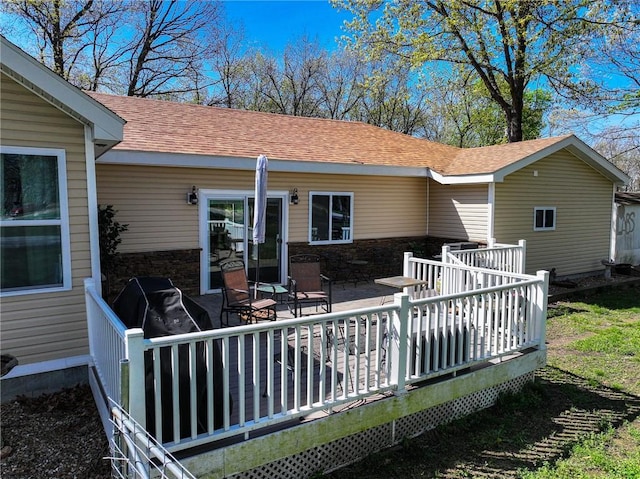 rear view of house with roof with shingles, a deck, and stone siding