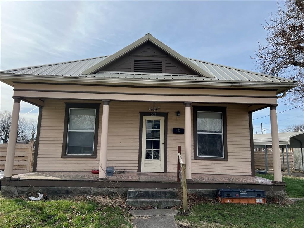 206 W 4th St, Norborne, MO 64668 - shotgun-style home featuring a porch, metal roof, and fence