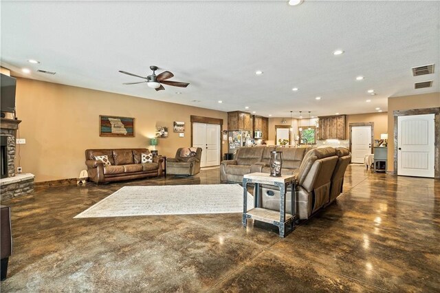 living area featuring finished concrete floors, ceiling fan, recessed lighting, a stone fireplace, and baseboards