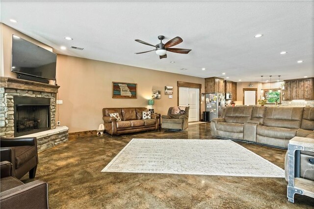 living room featuring concrete flooring, ceiling fan, recessed lighting, a stone fireplace, and baseboards