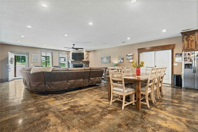dining room with a ceiling fan, finished concrete flooring, a stone fireplace, recessed lighting, and a textured ceiling