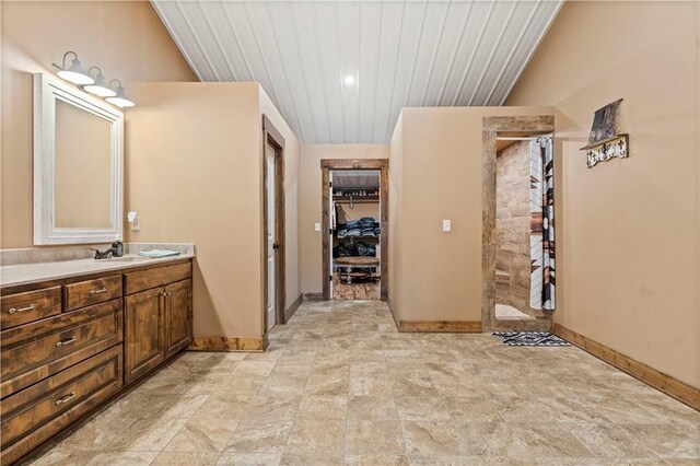 full bath with tiled shower, baseboards, wooden ceiling, stone finish flooring, and vanity