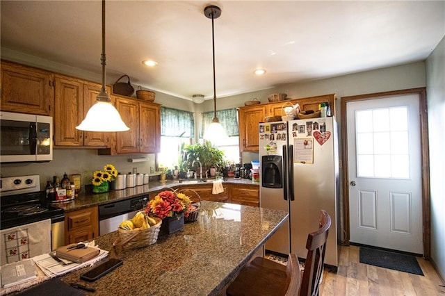 10875 SE 54th Hwy, Collins, MO 64738 - kitchen with stainless steel appliances, brown cabinets, light wood-type flooring, a kitchen bar, and decorative light fixtures