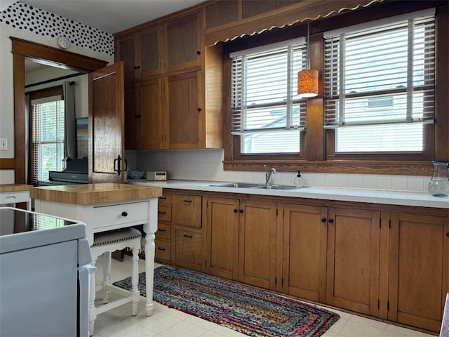 kitchen with light flooring, brown cabinetry, tasteful backsplash, stove, and a sink