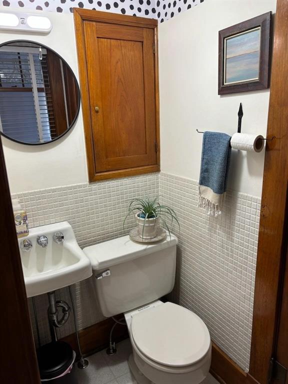 bathroom with a wainscoted wall, tile walls, toilet, and a sink