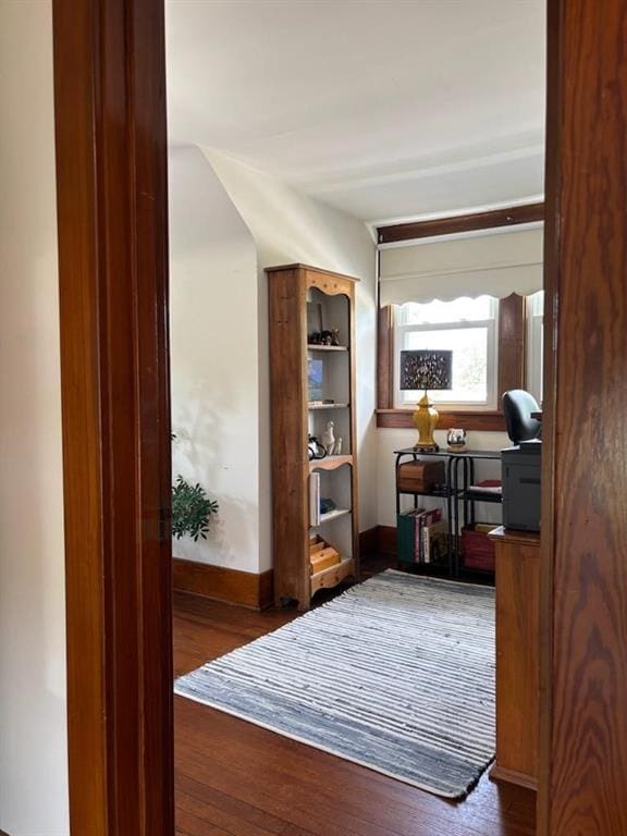 hallway with wood finished floors, baseboards, and a desk