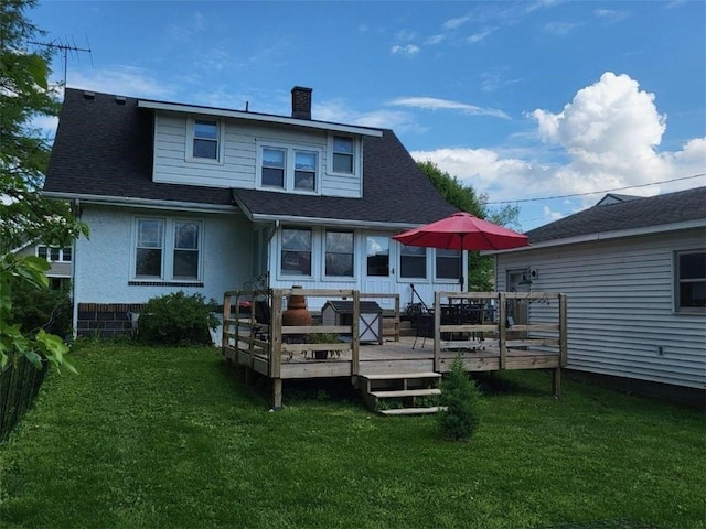 back of property featuring a chimney, a deck, a lawn, and roof with shingles