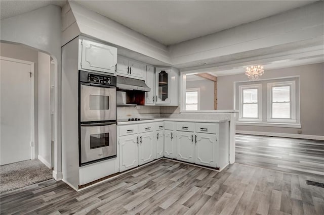 628 S Huttig Ave, Independence, MO 64053 - kitchen with double oven, light countertops, under cabinet range hood, light wood finished floors, and white cabinetry