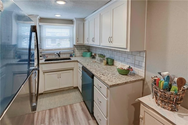 kitchen with a sink, dishwasher, light wood-style floors, decorative backsplash, and white cabinets