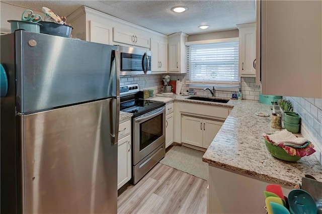 kitchen with appliances with stainless steel finishes, a sink, light wood-style flooring, a textured ceiling, and white cabinetry