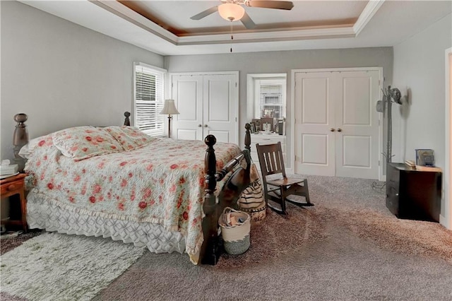 bedroom with a raised ceiling, carpet floors, two closets, and ceiling fan