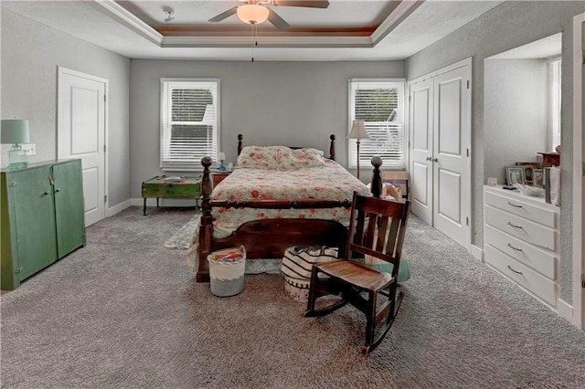 carpeted bedroom with a tray ceiling, ceiling fan, and baseboards