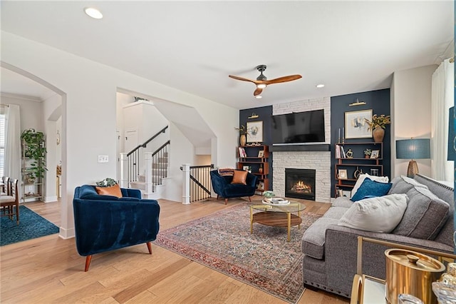 18873 W 168th Ter, Olathe, KS 66062 - living room with arched walkways, a ceiling fan, light wood-style floors, a large fireplace, and stairs