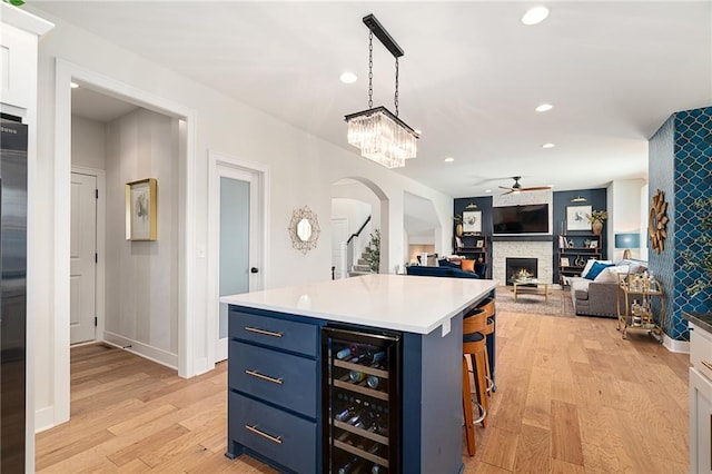 18873 W 168th Ter, Olathe, KS 66062 - kitchen with wine cooler, blue cabinetry, arched walkways, a ceiling fan, and a stone fireplace