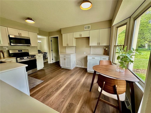 kitchen featuring stainless steel appliances, white cabinetry, dark wood-style flooring, backsplash, and a textured ceiling