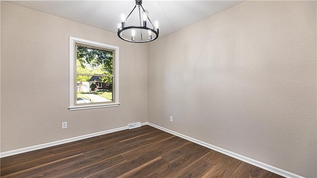 spare room with a chandelier, dark wood-style floors, and baseboards