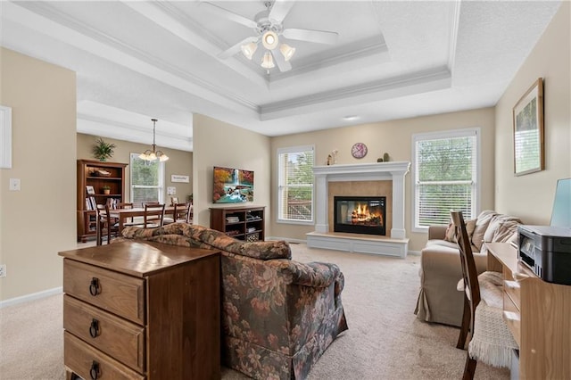 carpeted living room with a raised ceiling, a ceiling fan, a glass covered fireplace, baseboards, and crown molding