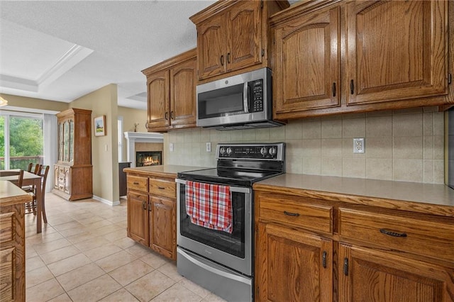 kitchen with stainless steel appliances, baseboards, tasteful backsplash, light tile patterned flooring, and brown cabinetry