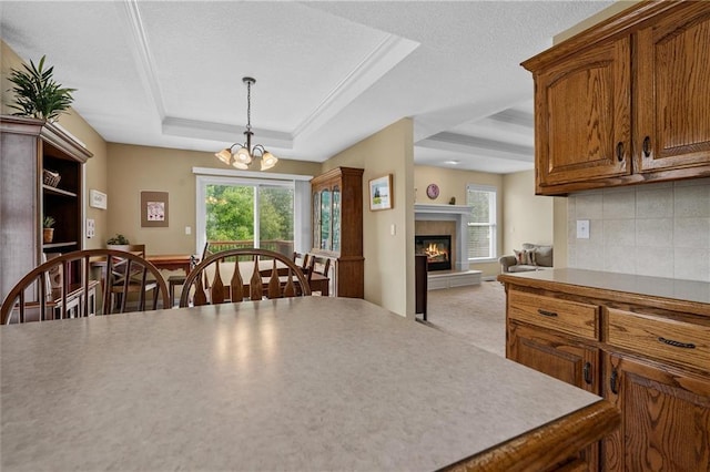 kitchen featuring a glass covered fireplace, decorative backsplash, a raised ceiling, light countertops, and decorative light fixtures