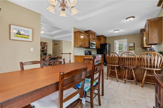 dining area with a raised ceiling, ornamental molding, a chandelier, light tile patterned floors, and a ceiling fan