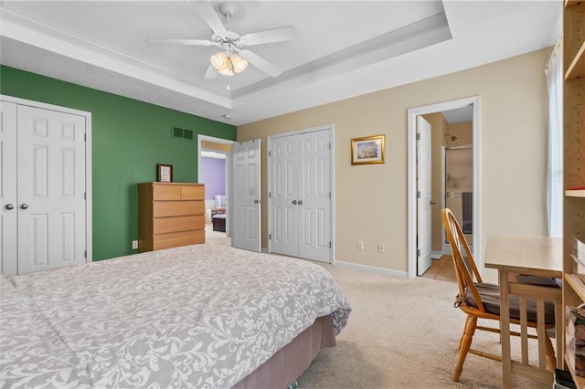 bedroom featuring a tray ceiling, light carpet, two closets, baseboards, and a ceiling fan