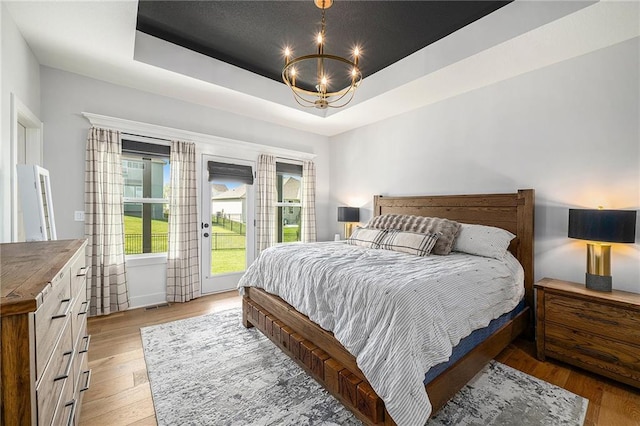 1309 NW 107th Ter, Kansas City, MO 64155 - bedroom with access to exterior, light wood-style flooring, a chandelier, and a raised ceiling