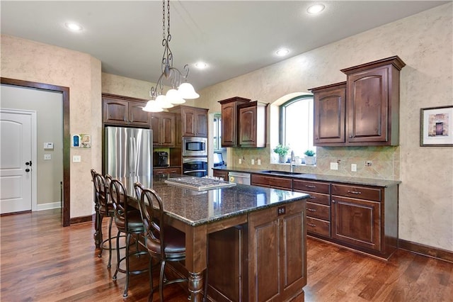 kitchen with stainless steel appliances, a sink, dark wood finished floors, a kitchen breakfast bar, and baseboards