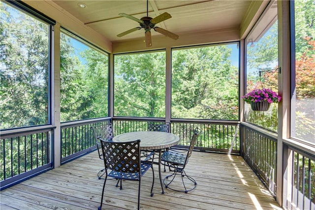 sunroom / solarium with ceiling fan, outdoor dining space, and view of wooded area