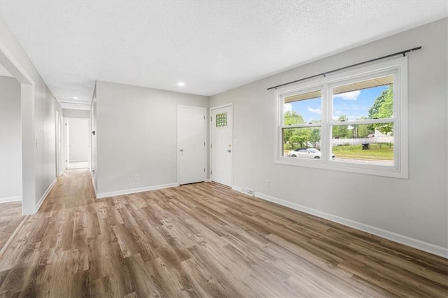 unfurnished living room featuring baseboards, light wood-type flooring, recessed lighting, and a textured ceiling