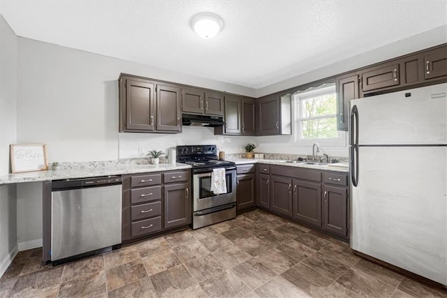 kitchen with appliances with stainless steel finishes, under cabinet range hood, a sink, baseboards, and dark brown cabinetry