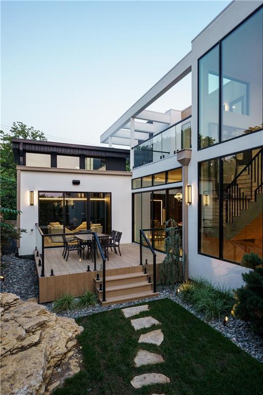 rear view of property featuring a balcony, a wooden deck, outdoor dining space, and stucco siding