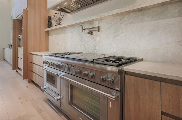 kitchen featuring double oven range, tasteful backsplash, light countertops, and light wood-type flooring