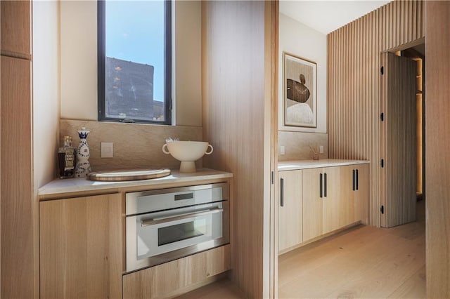 kitchen with oven, light countertops, light brown cabinetry, light wood-style floors, and backsplash