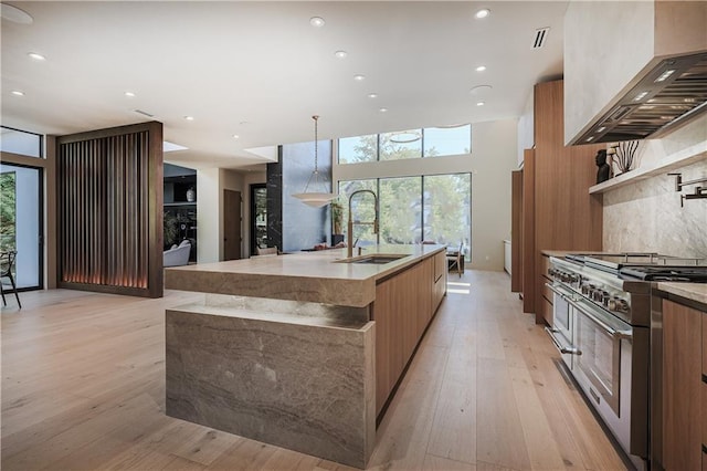 kitchen with modern cabinets, double oven range, a sink, brown cabinetry, and custom exhaust hood