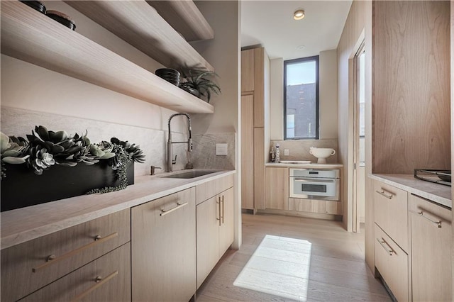 kitchen featuring wall oven, open shelves, a sink, light wood-type flooring, and decorative backsplash