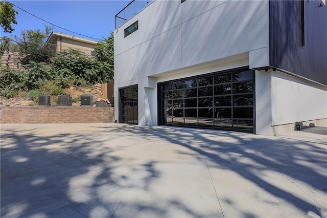 view of property exterior with a garage, driveway, central air condition unit, and stucco siding