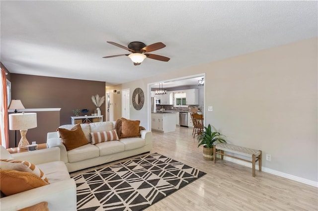 living room with ceiling fan, light wood finished floors, a chandelier, and baseboards