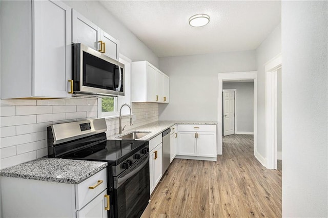2206 E 30th St, Kansas City, MO 64109 - kitchen with appliances with stainless steel finishes, light wood-style flooring, decorative backsplash, light stone countertops, and white cabinets