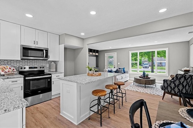 11424 W 68th Pl, Shawnee, KS 66203 - kitchen with appliances with stainless steel finishes, open floor plan, white cabinetry, light wood-type flooring, and a kitchen breakfast bar