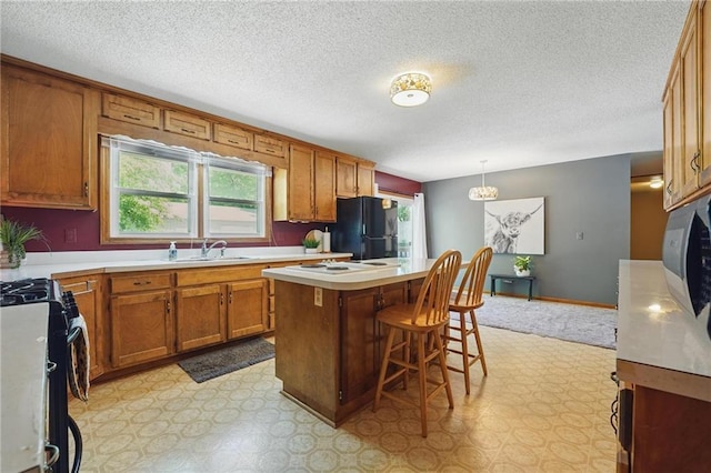 kitchen featuring freestanding refrigerator, brown cabinetry, gas range, plenty of natural light, and a textured ceiling