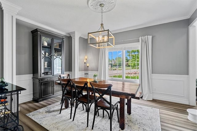 19600 W 98th St, Lenexa, KS 66220 - dining room with crown molding, a chandelier, wainscoting, wood finished floors, and decorative columns