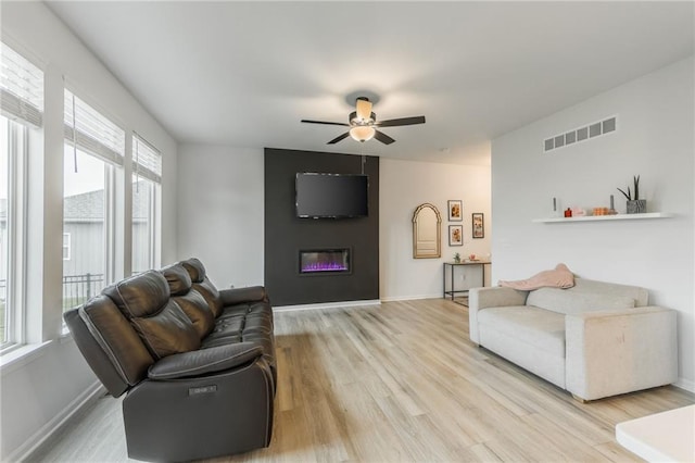 living area featuring ceiling fan, light wood-style flooring, a glass covered fireplace, and baseboards