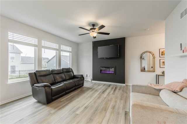living area with a glass covered fireplace, light wood-type flooring, ceiling fan, and baseboards