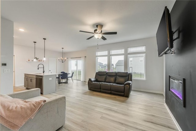 living area featuring a glass covered fireplace, ceiling fan, light wood-style floors, a chandelier, and baseboards
