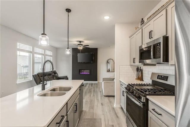 kitchen with stainless steel appliances, a sink, open floor plan, light countertops, and recessed lighting